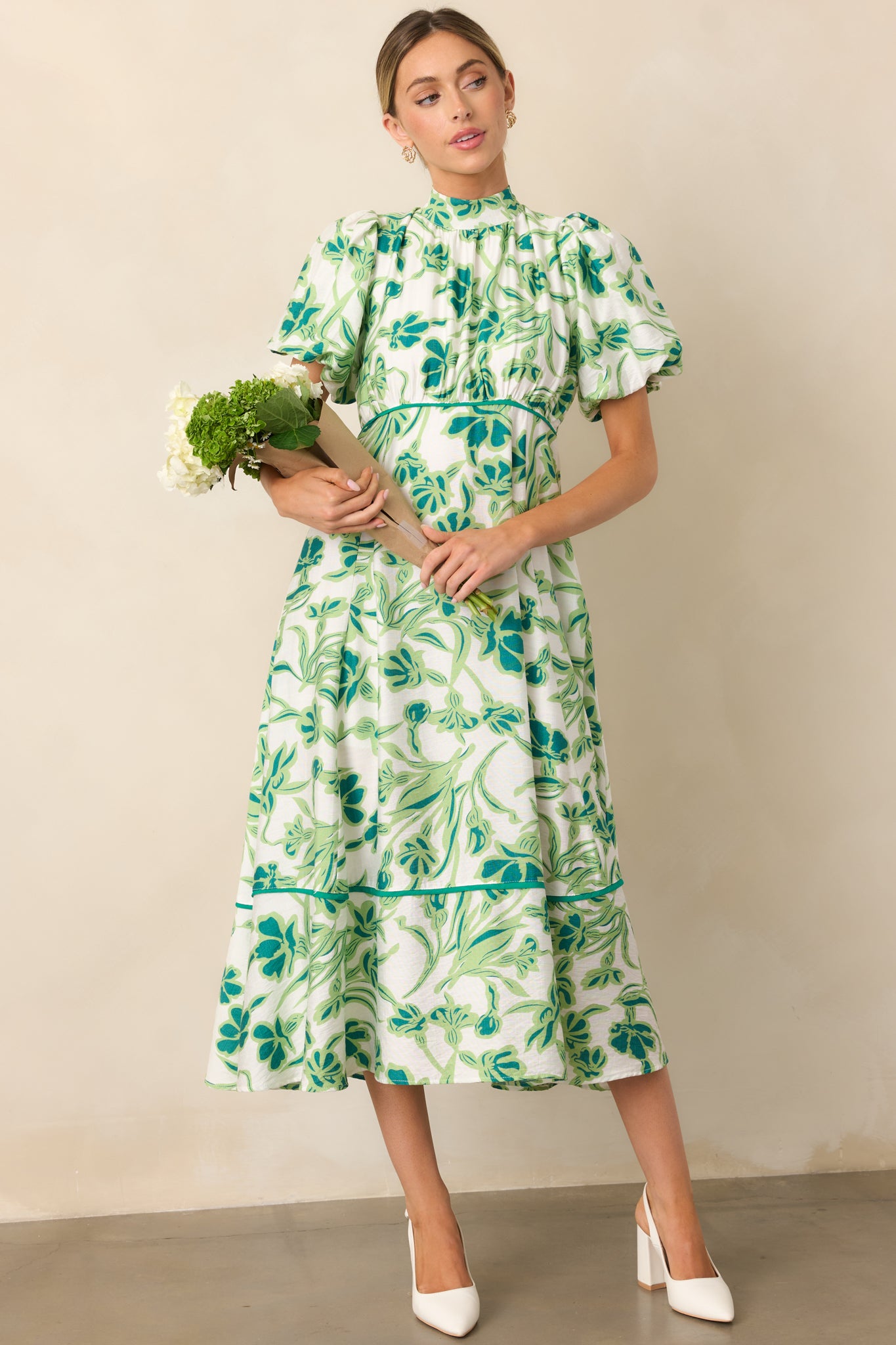 A green midi dress featuring a high self-tie mock neckline, a delicate floral print, a smocked back, and puff sleeves.