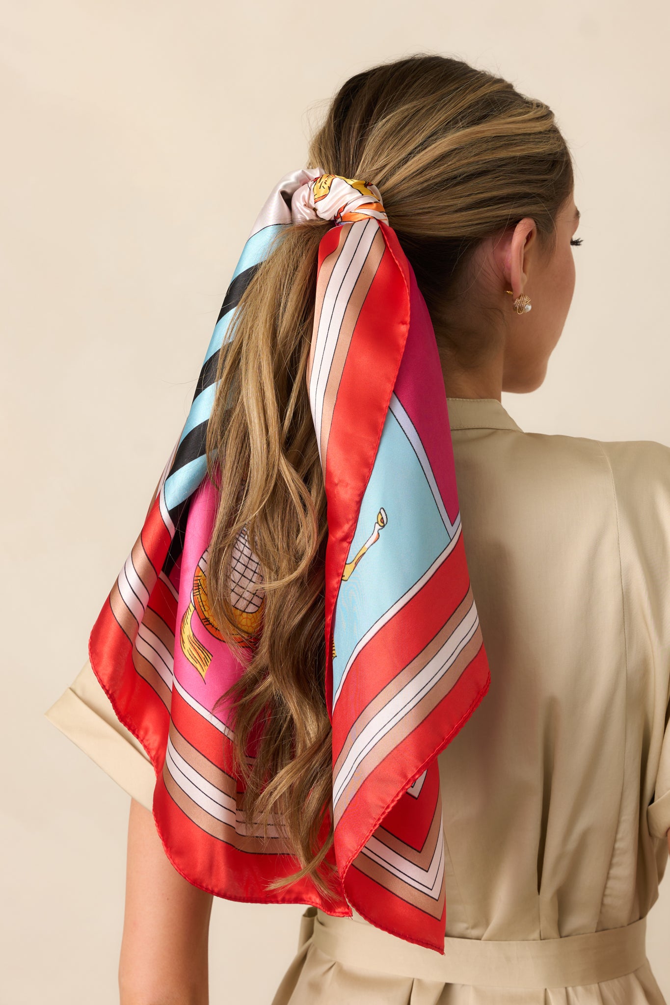A vibrant red hair scarf with a striking design of horses, accented by shades of ivory, pink, orange, and blue. The red trim frames the scarf, enhancing the colorful pattern.