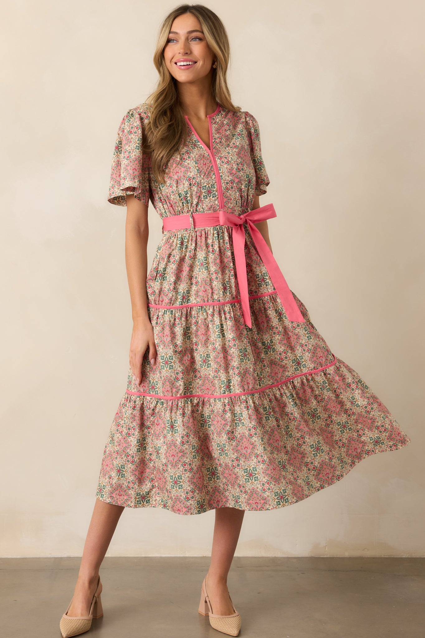 A pink midi dress featuring a notch v-neckline, short butterfly sleeves, an optional self-tie belt, and a geometric floral print.