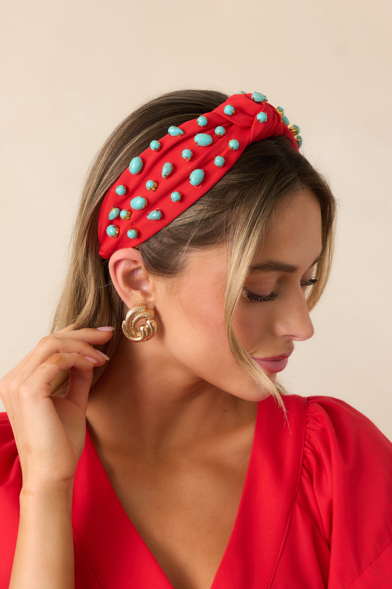 This red headband features a black headband base, a red cloth material decorated with gold bordered turquoise beading, and a knotted top.