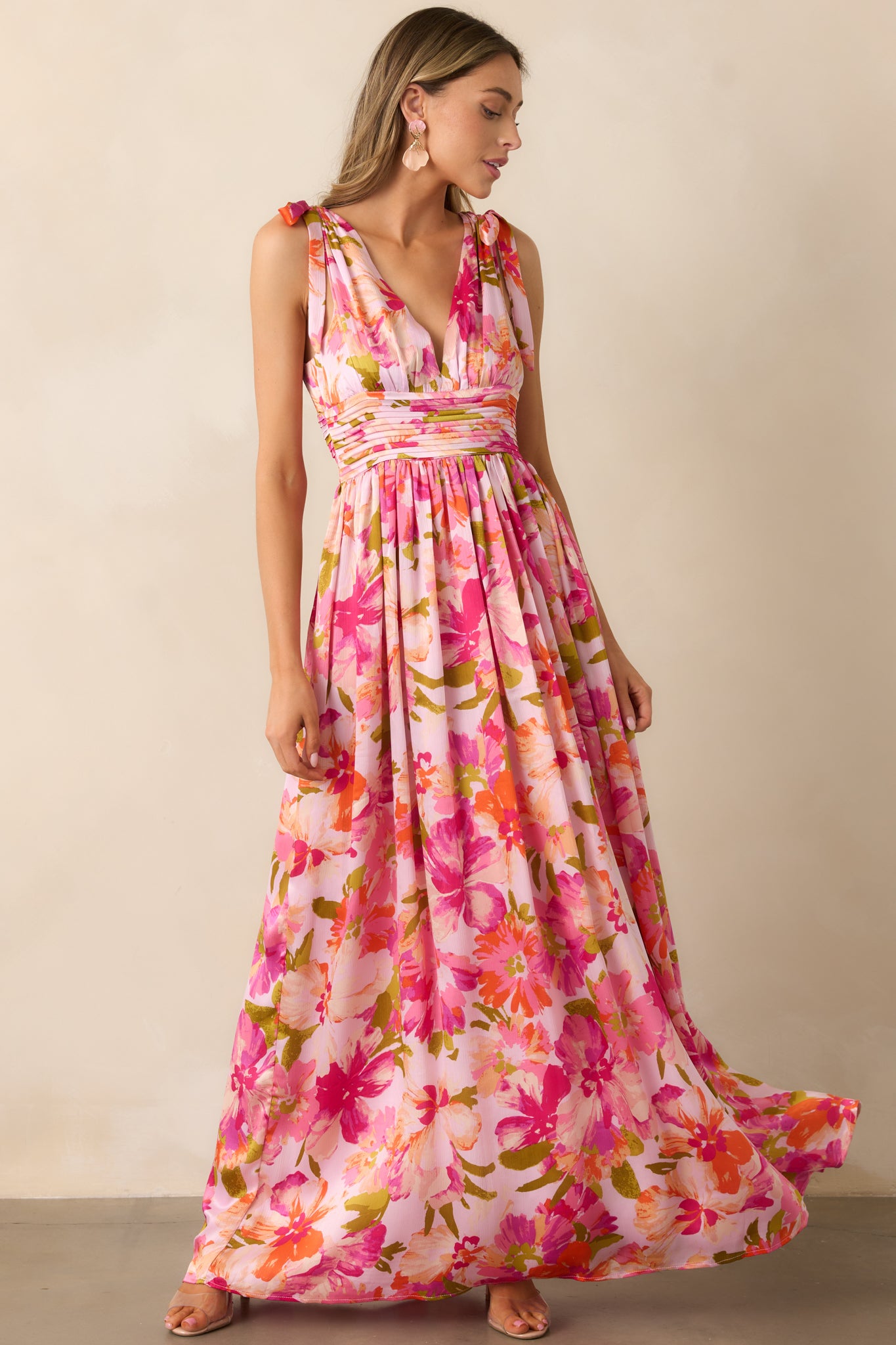 A pink maxi dress with a deep v-neckline, bow details on both shoulders, and a flowing silhouette.