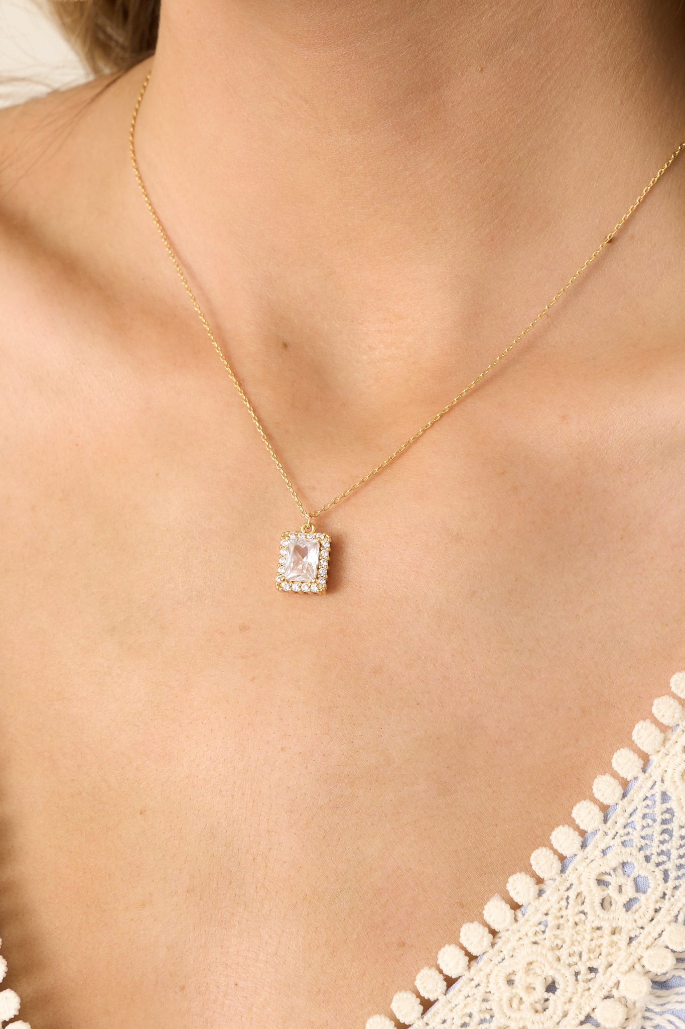 A highly detailed view of the pendant, emphasizing the facets of the emerald-cut rhinestone, the shimmering pave halo, and the way the gold setting enhances the brilliance of the stones.