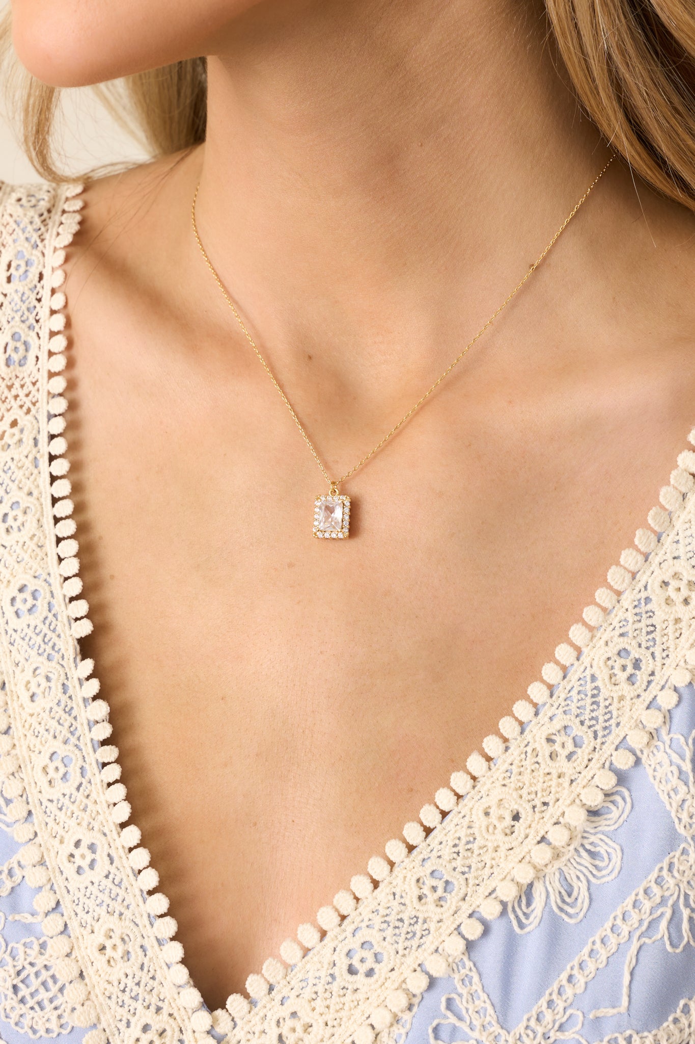 A close-up view of the gold necklace's rectangular emerald-cut rhinestone, surrounded by a halo of small pave rhinestones, highlighting its sparkle and intricate detailing.