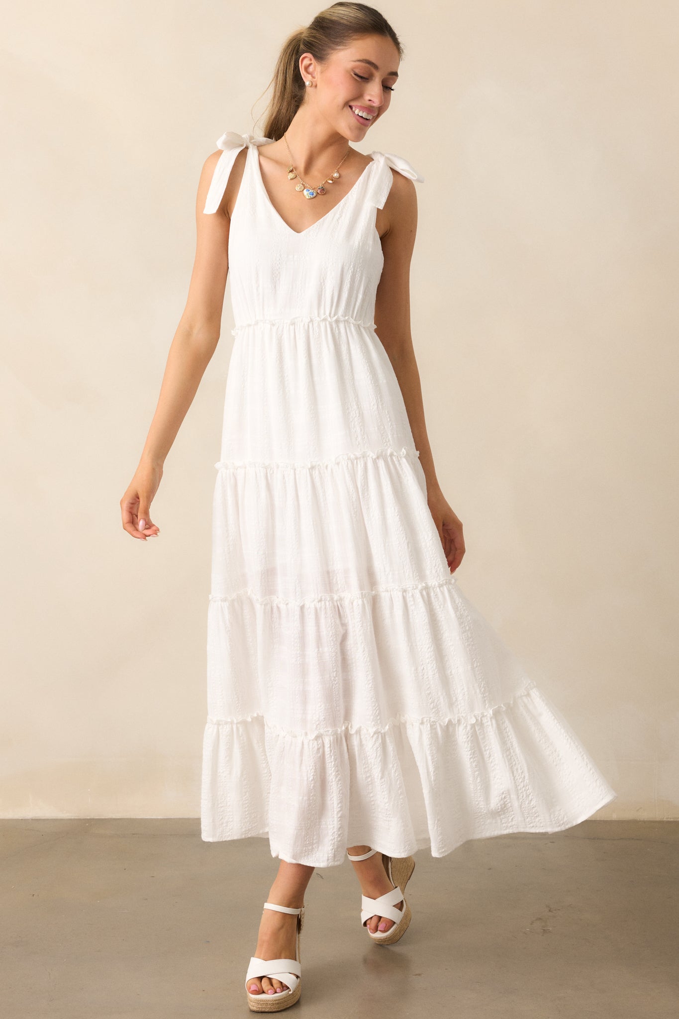 A delicate ivory dress crafted from lightweight textured fabric, featuring a flattering v-neckline, tiered skirt, and playful ruffles for added movement.
