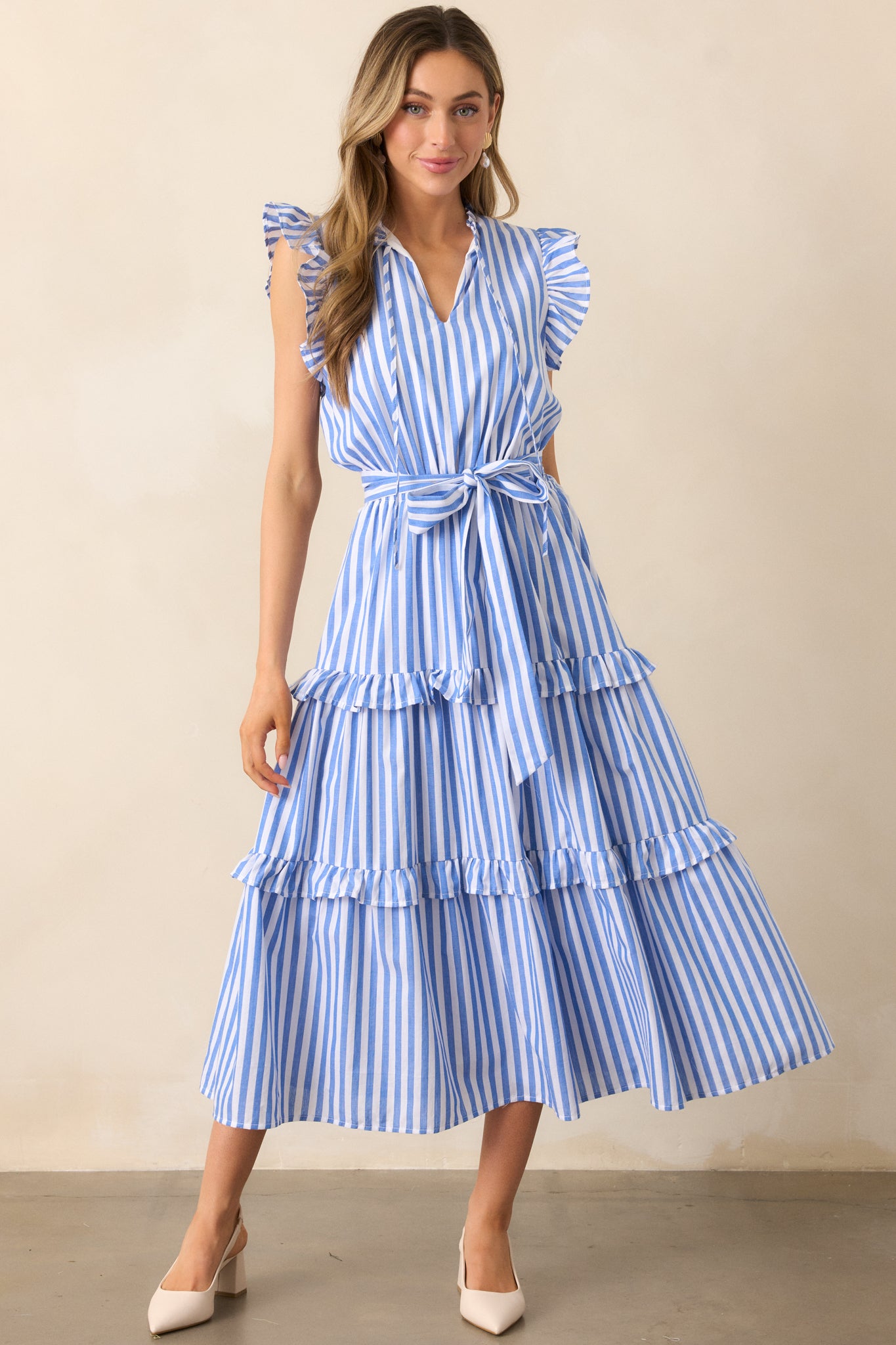 A blue striped dress with a notch V-neckline, flutter cap sleeves, and a tiered skirt with ruffle detailing for a playful, feminine look.