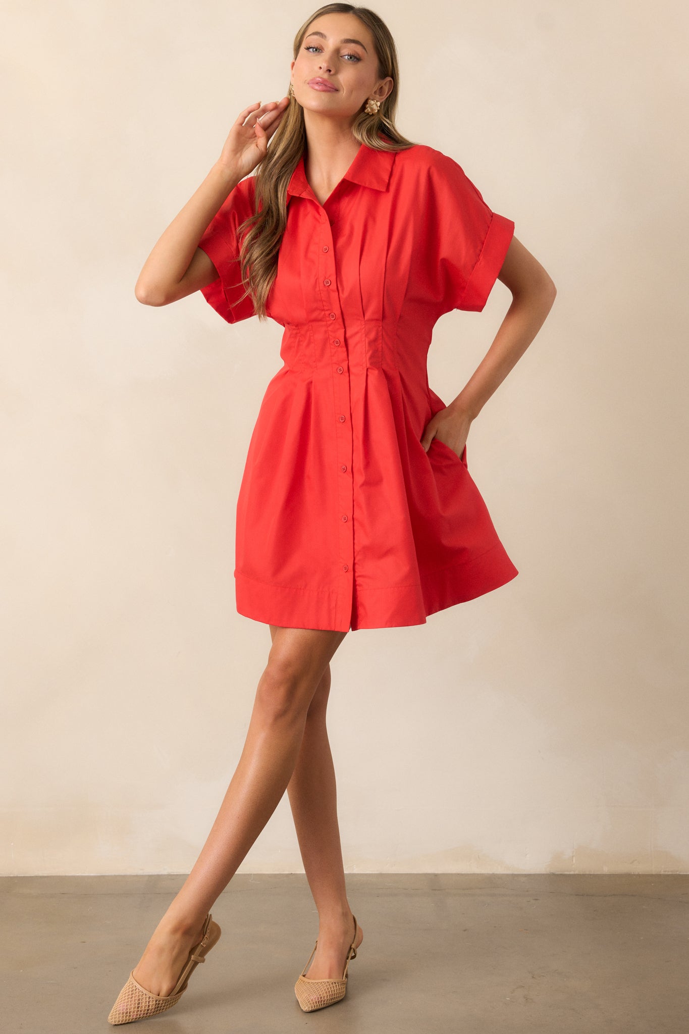 This red mini dress features a classic collared neckline, functional button front, and pleated waist gathering for a flattering, structured silhouette.