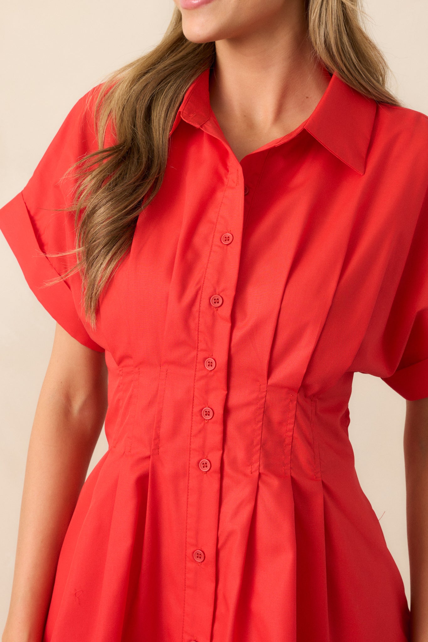 The pleated waist gathering and button-front details create a polished and structured look, elevating the classic red mini dress.