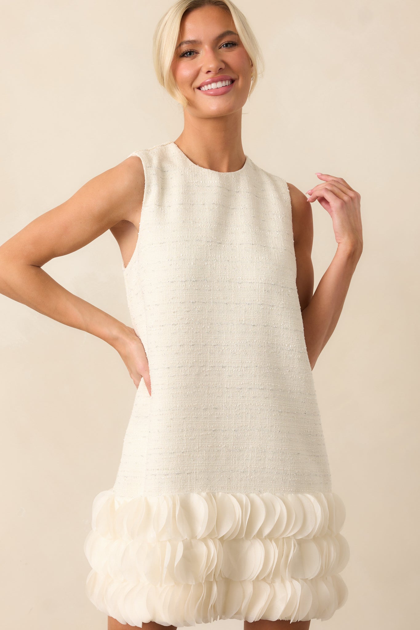 The ivory mini dress featuring a round neckline, silver tinsel details, and a voluminous 3D petal bottom tier.