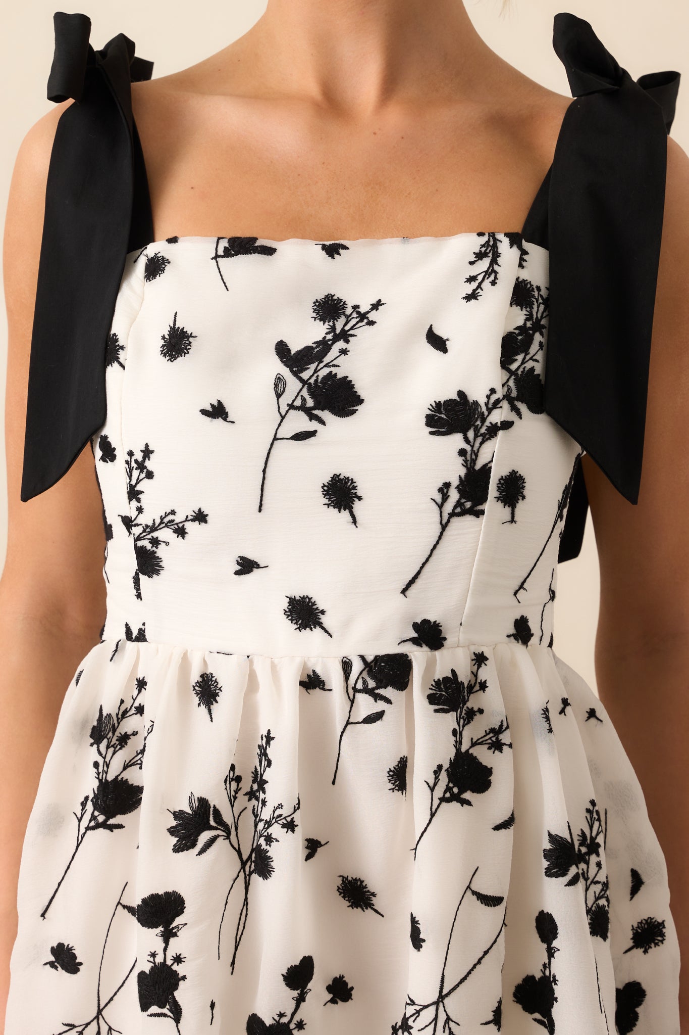 A close-up of the black floral embroidery on the ivory dress, showcasing the detailed stitching and textured design.