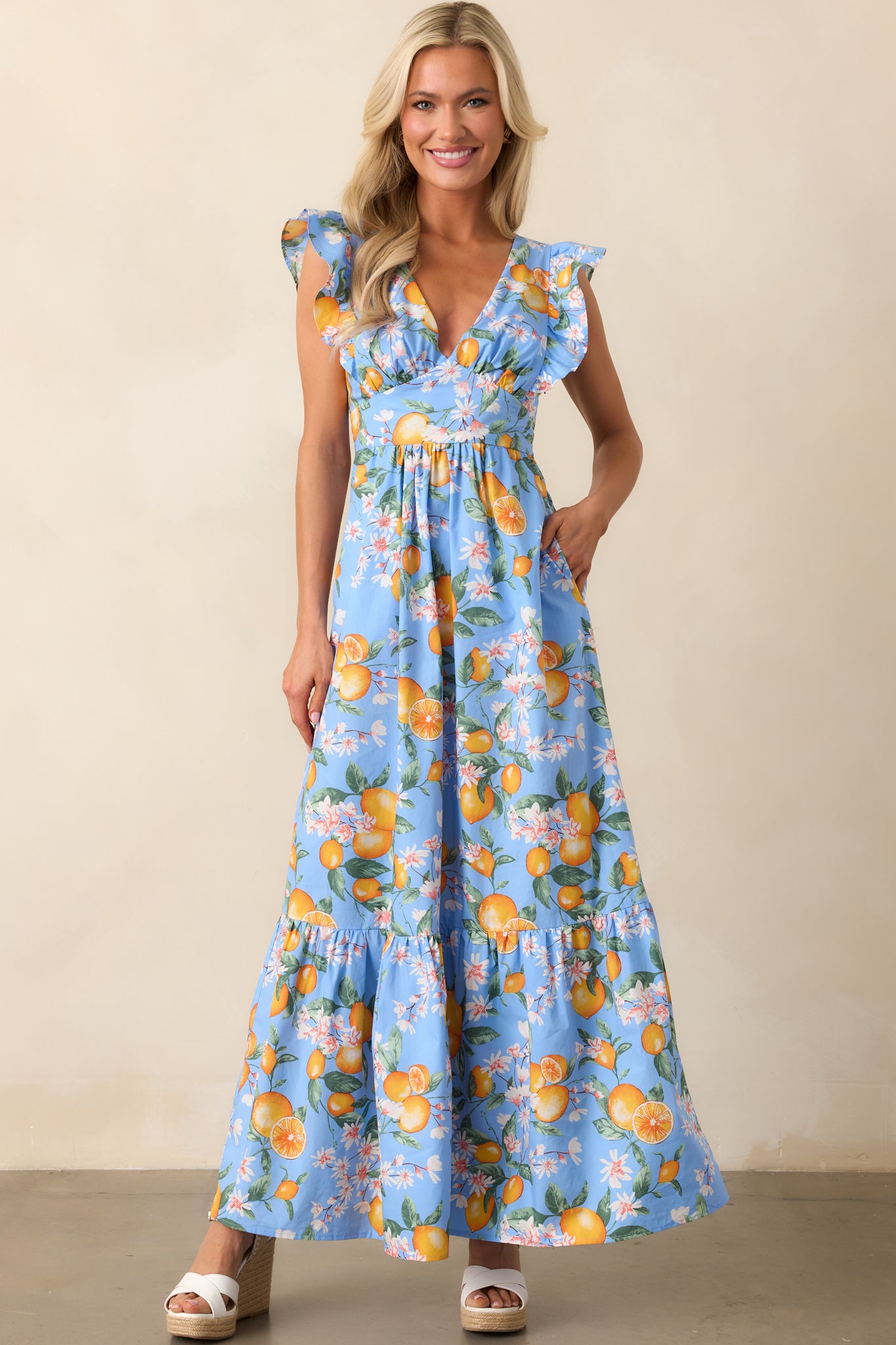A blue maxi dress featuring a playful floral lemon print, deep V-neckline, and short flutter sleeves, perfect for a breezy look.