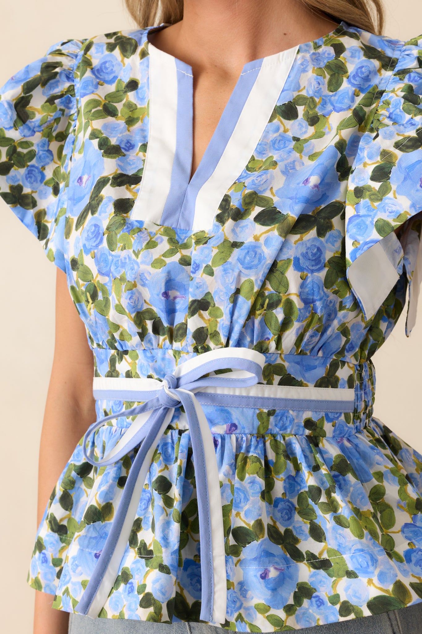 A close-up of the intricate bow front detail and notch v-neckline of the blue floral top, highlighting the light, airy fabric and delicate floral print.
