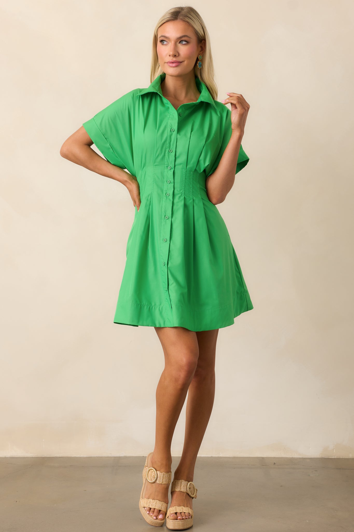 A vibrant kelly green mini dress featuring a collared neckline, button front design, and pleated skirt, paired with a fitted waistband for a flattering silhouette.