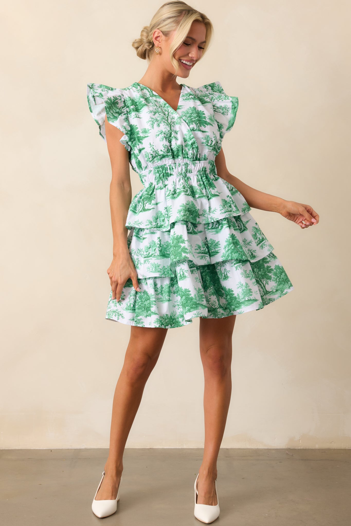 This eden green mini dress features a delicate v-neckline, fluttery ruffle sleeves, and a tiered skirt that adds volume and movement.